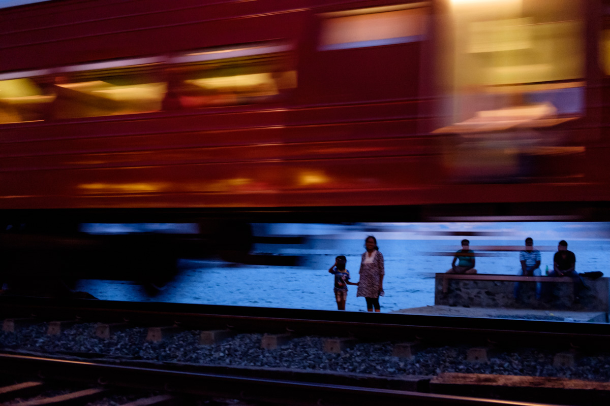 A woman and child wait to cross the tracks by the sea.