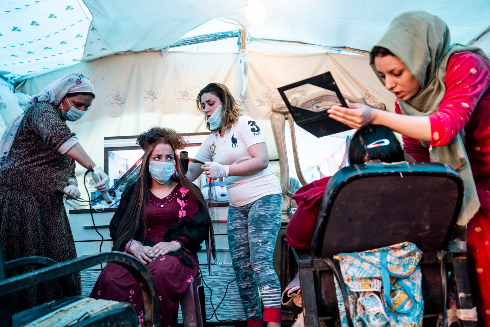 Buthena (center, in the white tshirt) straightens the hair of a bride in her new salon with her mother, while another customer gets her makeup done. The salon is a space for women to gather, chat and care for themselves. Photo by Charlene Winfred/Preemptive Love